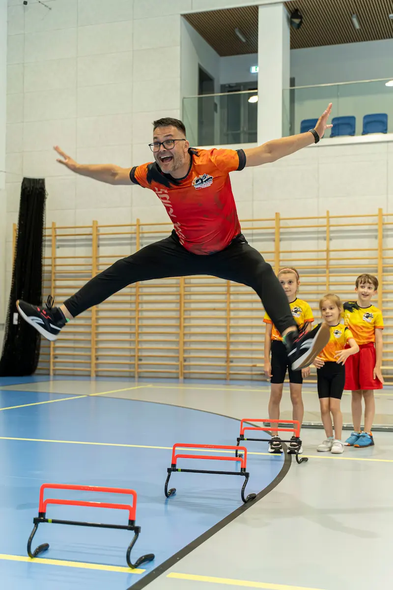 Trener Ninja Kids robi wielki wyskok nad przeszkodami.