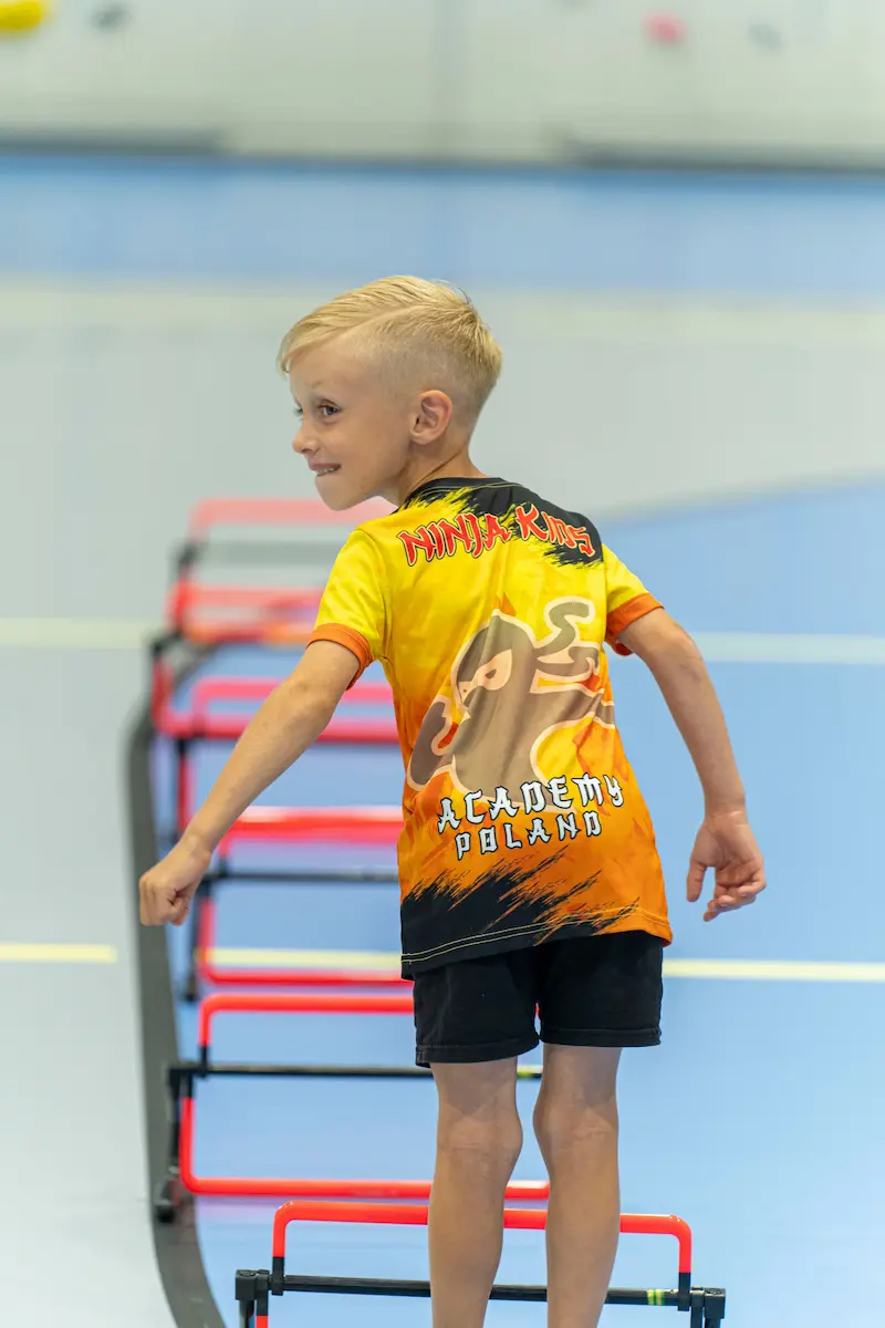 Mały chłopiec patrzy do tyłu w trakcie pokonywania przeszkód w Ninja Kids Academy